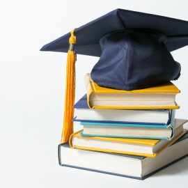 Books from scholarship stacked with graduation cap