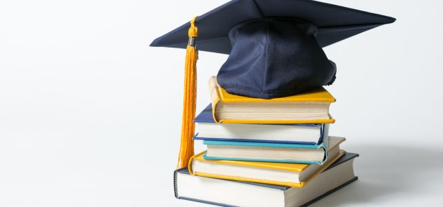 Books from scholarship stacked with graduation cap